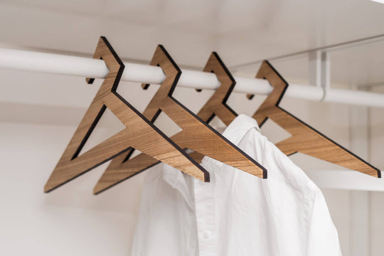 Geometric wooden hangers with a triangular design and rich walnut finish, holding a white shirt in a minimalist closet.