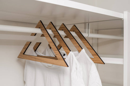 Set of wooden hangers in ash wood finish, featuring a sharp geometric design, holding white t-shirts in an organized closet.