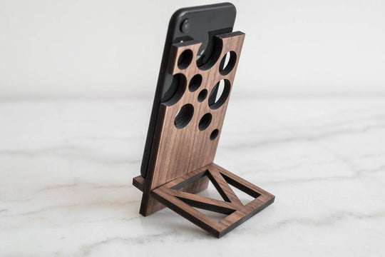 Wooden phone stand with a unique geometric design featuring circular cutouts, holding a phone at an angle on a smooth surface.