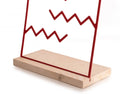 Red zigzag metal jewelry holder on a natural wood base, simple and minimalistic design.