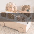 Child playing inside a minimalist wooden bus-shaped storage box, designed with natural wood and white accents. Ewart Woods branding is visible with the slogan &