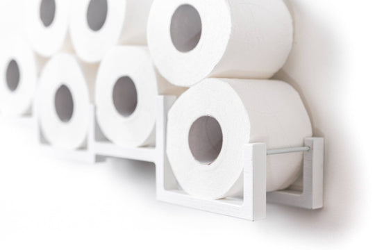 Close-up of a white wall-mounted toilet paper holder, holding seven rolls of toilet paper. The holder has a unique geometric design with individual frames for each roll.