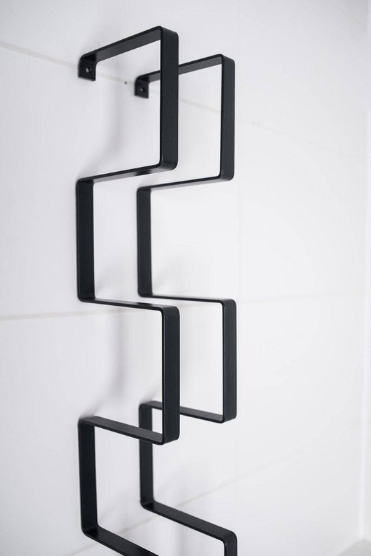 Close-up of a black geometric wall-mounted organizer with square frames, showcasing a modern design for holding multiple toilet paper rolls.